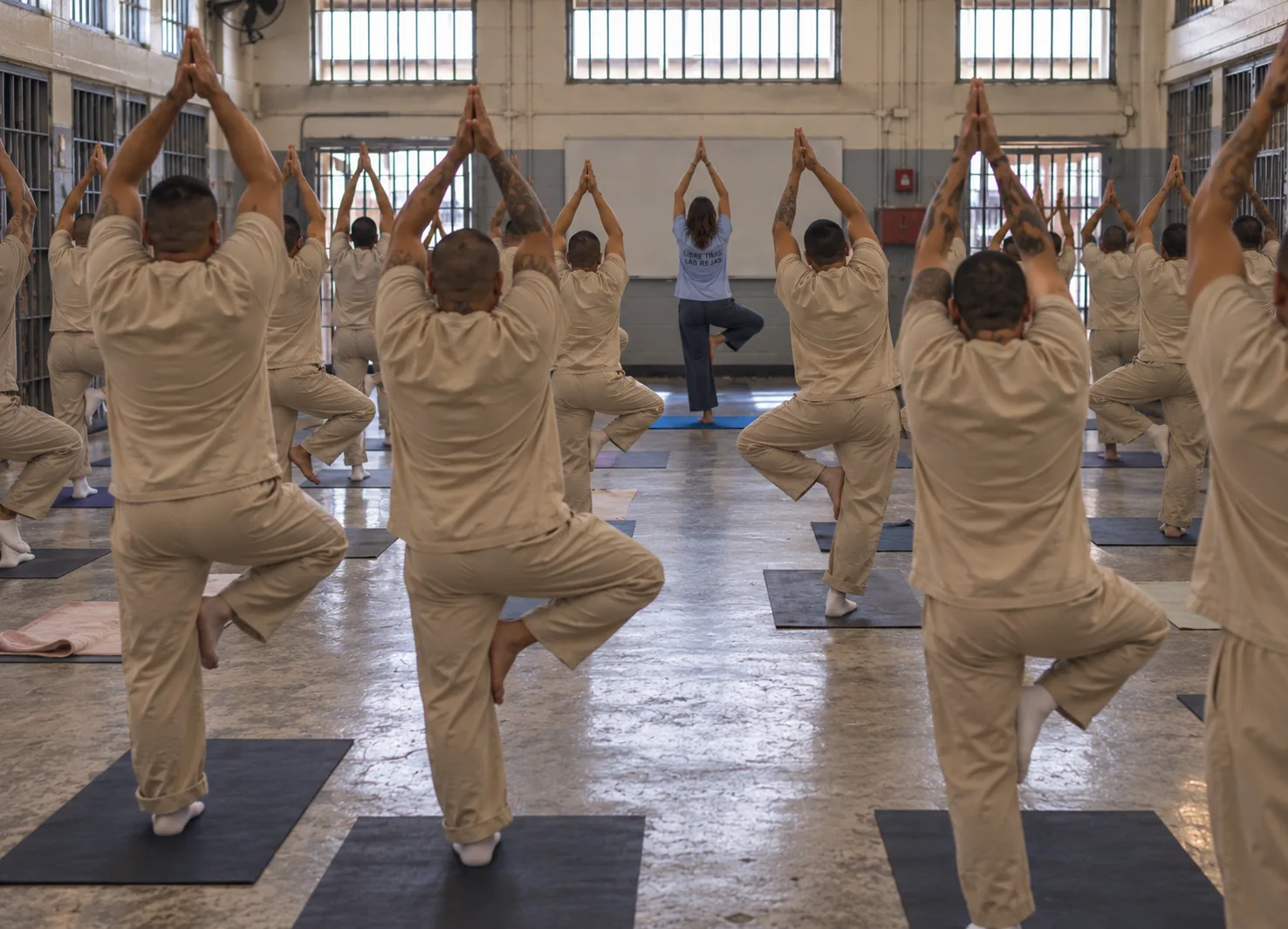 Personas privadas de la libertad, de espaldas, sostienen la postura del árbol durante una clase de yoga.