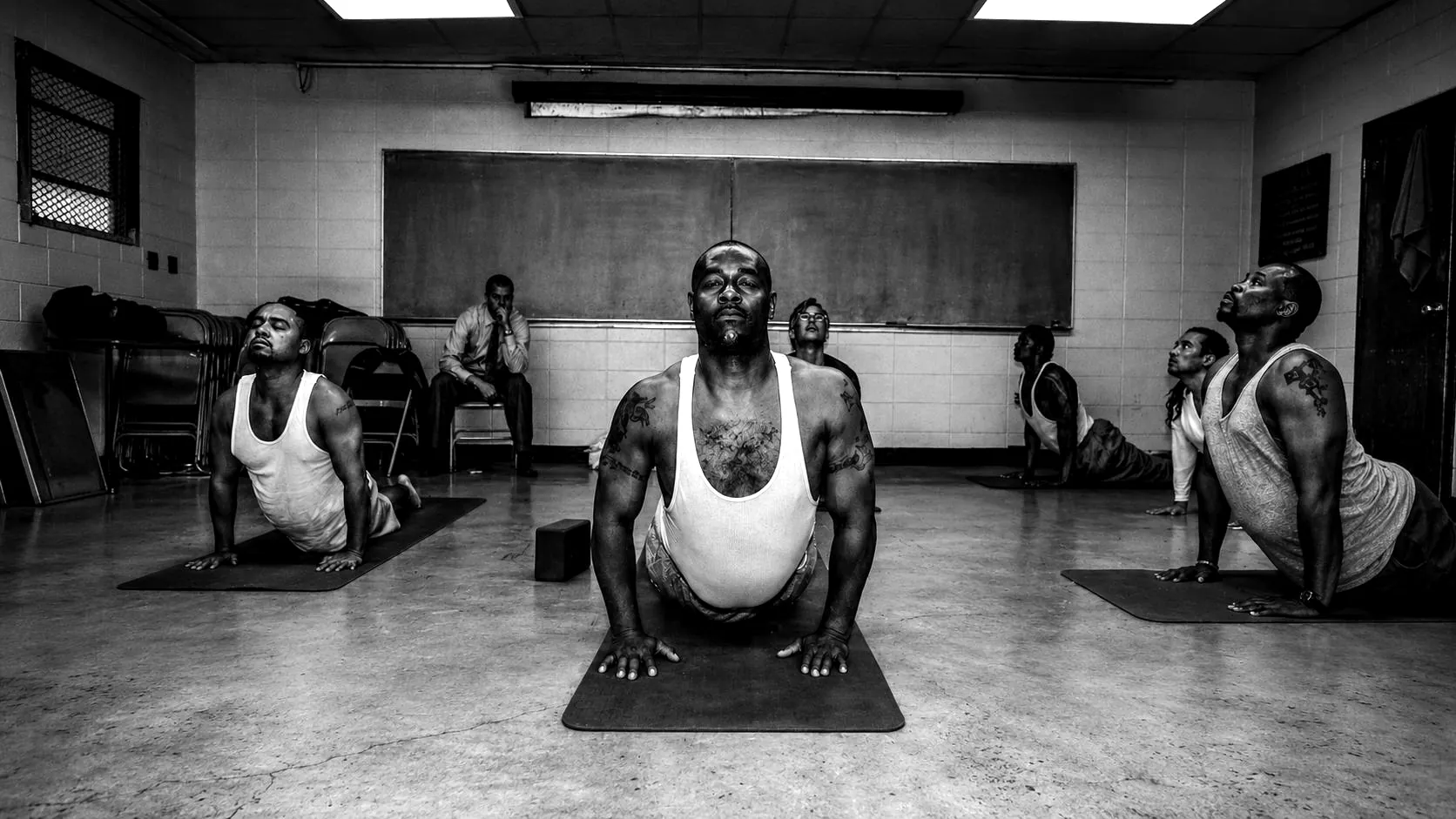Personas privadas de la libertad practican yoga sobre tapetes en un salón.