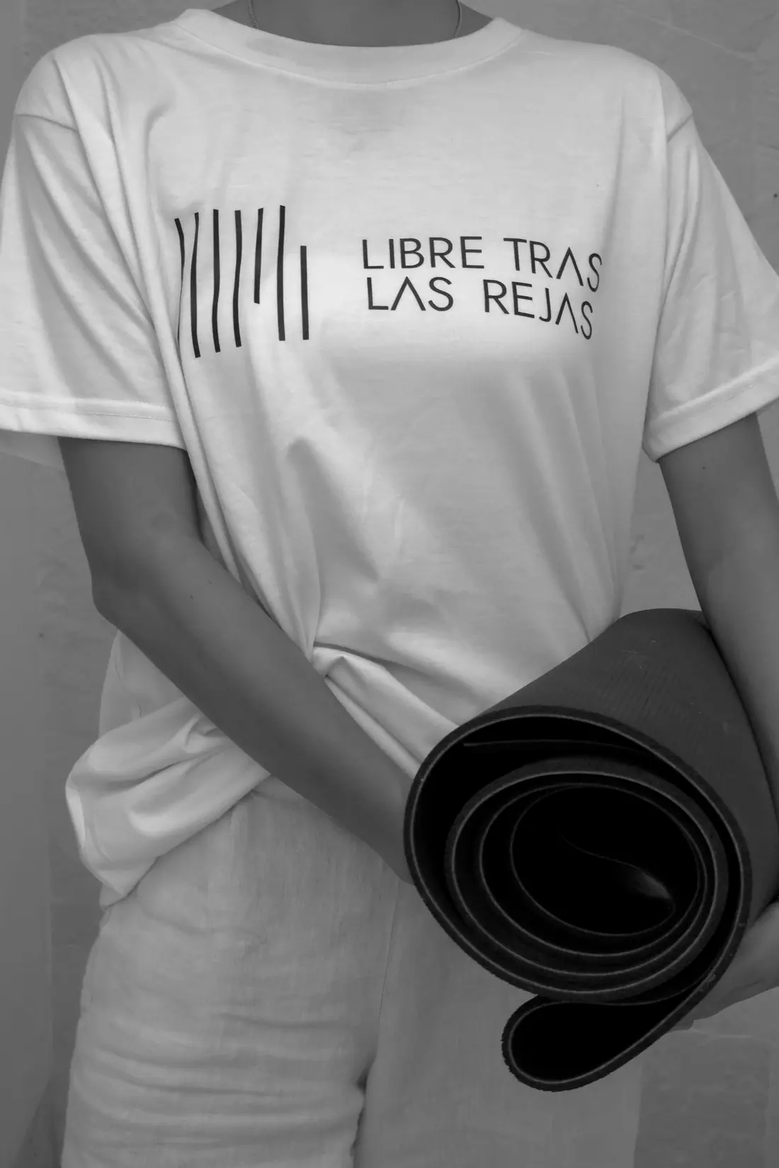 Persona con playera de Libre Tras las Rejas sostiene un tapete de yoga enrollado.
